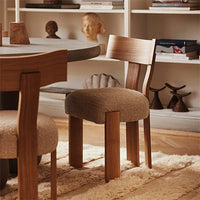 Brown upholstered chair with wooden legs, featuring a soft texture and warm, neutral tones against a cozy background.