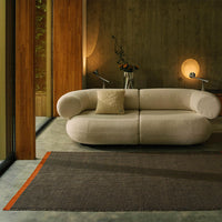 Neutral beige sofa with a textured surface and a striped black and orange rug, creating a modern, cozy aesthetic.