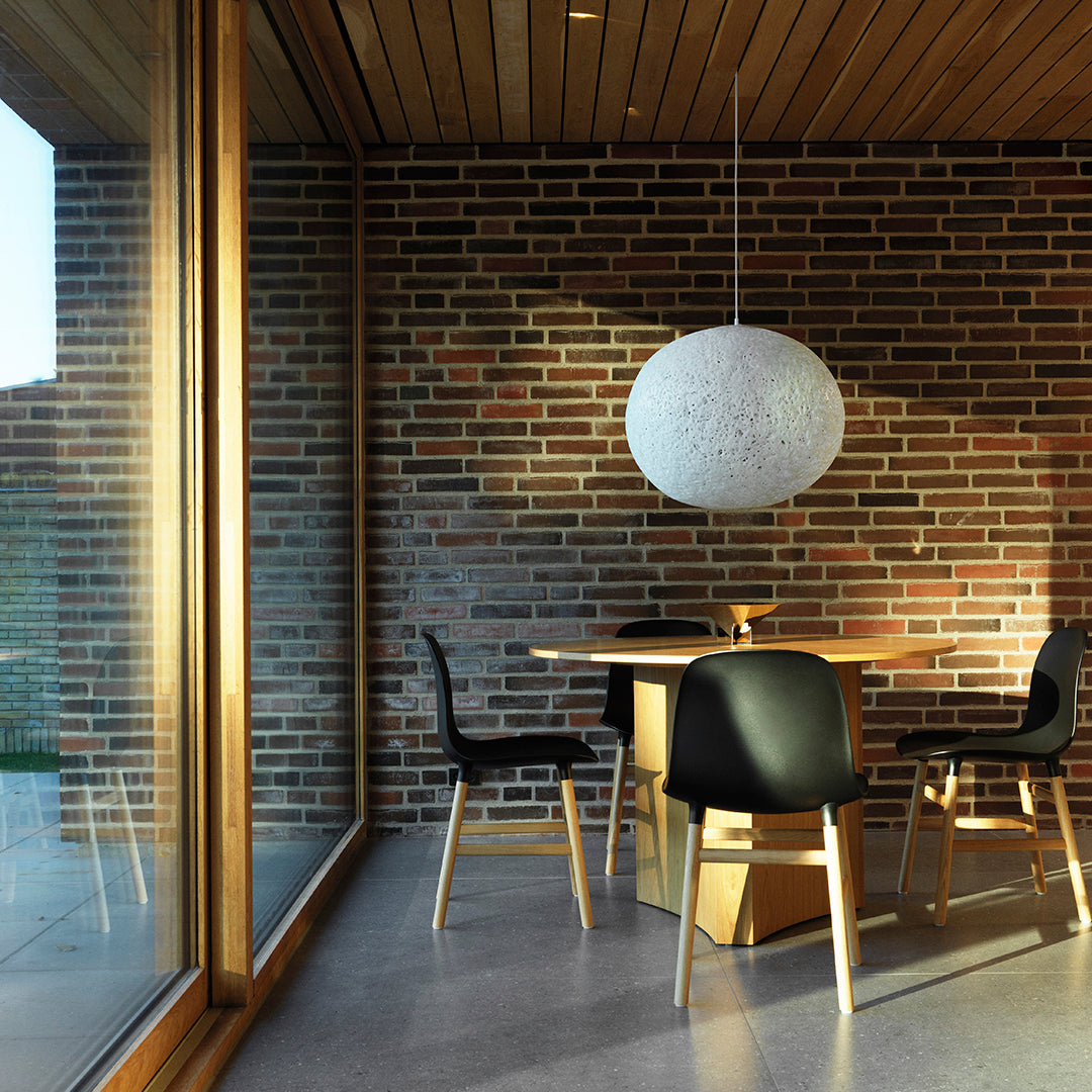 Modern dining room featuring earthy brown brick walls, sleek black chairs, and a textured white pendant light.