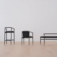 Black wooden chairs and bench with smooth black cushions against a light wood floor and neutral wall.