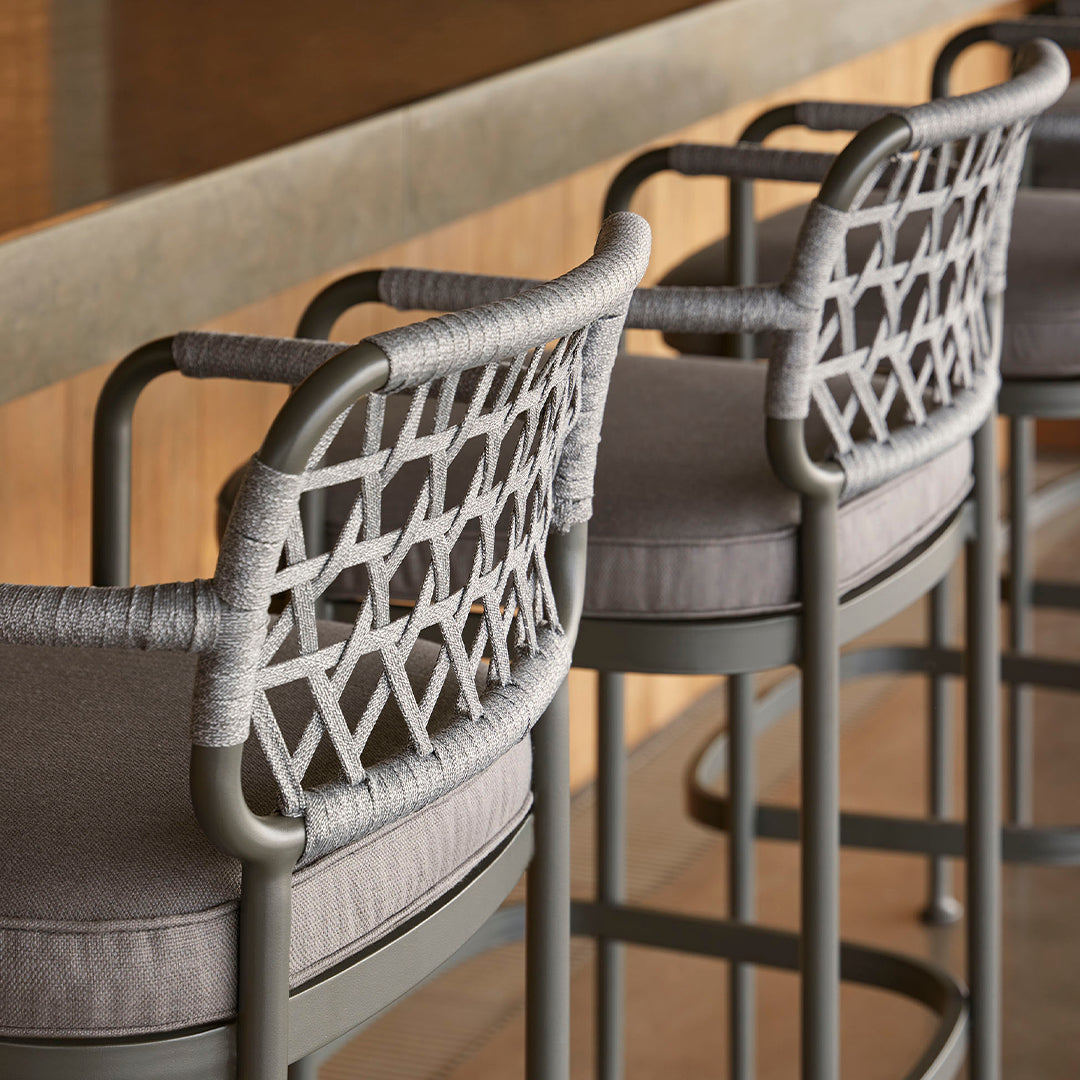 Gray woven bar stools with geometric patterns and light fabric cushions. Modern design for stylish seating.