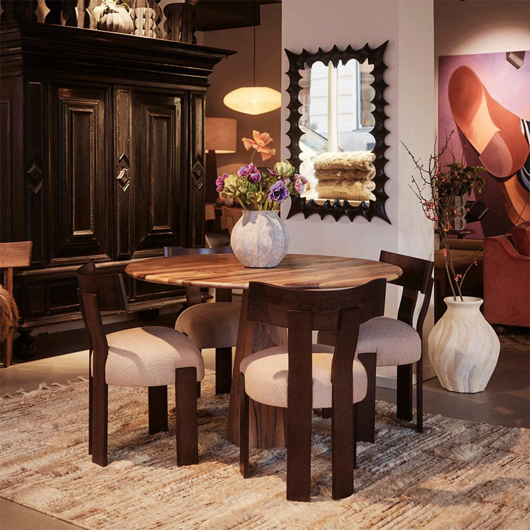 Wooden dining table with natural finish, beige upholstered chairs, and dark accents in a warm, inviting interior.