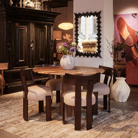 Wooden dining table with dark brown chairs, beige fabric upholstery, and a neutral-colored rug, complemented by a white vase.
