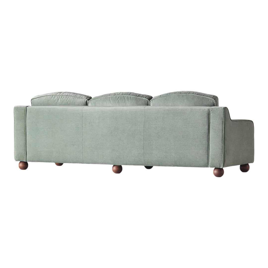 Green upholstered sofa with soft fabric and rounded wooden legs, showcasing a minimalist design.