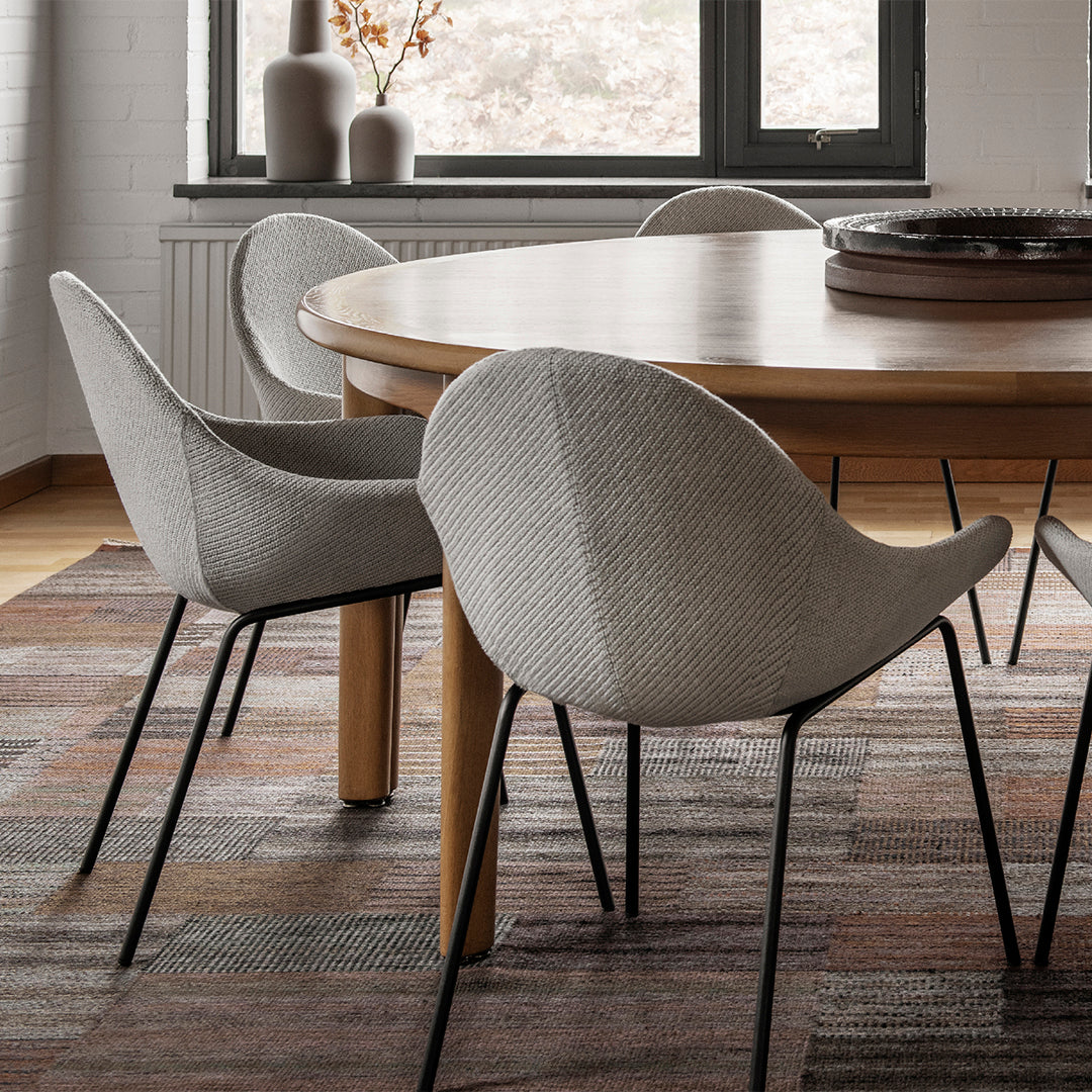 Gray textured chairs on a multicolored patterned rug with earthy tones and a wooden table. Modern interior design.