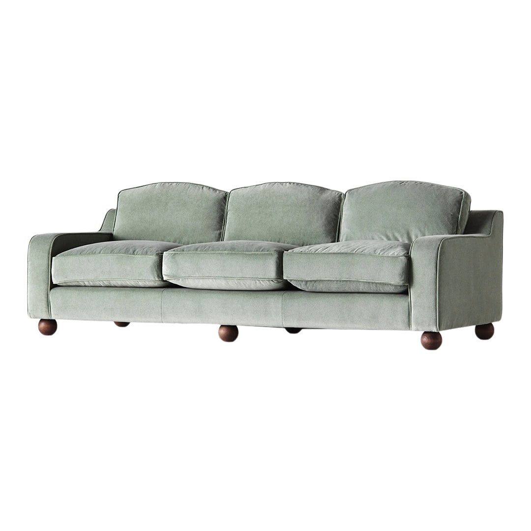 Sofa in soft sage green fabric with rounded cushions and dark wooden feet, offering a contemporary, cozy look.