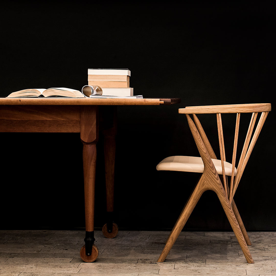 Wooden table and chair in natural tones against a black background, showcasing sleek lines and minimalistic design.