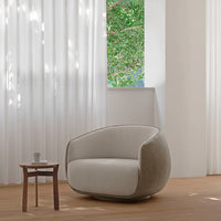 Modern beige armchair with a smooth texture, paired with a wooden table and bright white curtains, creating a serene ambiance.