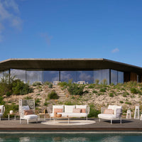 Modern outdoor furniture set featuring white cushions, pastel pink and beige accents against a natural green landscape.