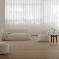 Soft white seating furniture against a light wood floor, paired with a neutral rug and sheer white curtains.