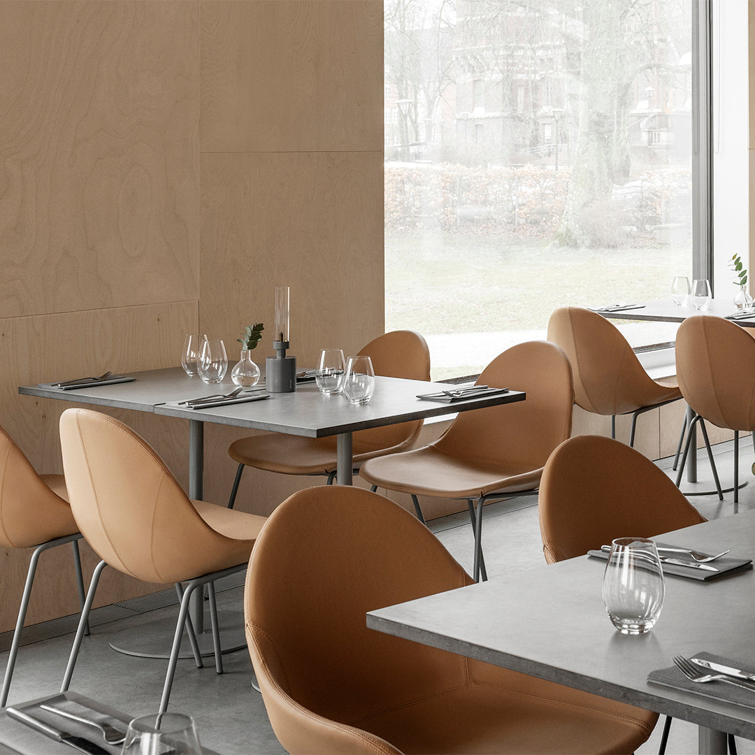 Modern dining space featuring soft tan chairs and sleek gray tables against a neutral wood backdrop.