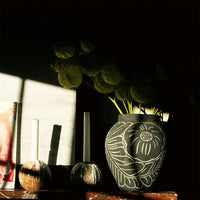 Black vase with white floral patterns, accented by green leaves and soft shadows, creating an elegant, serene display.