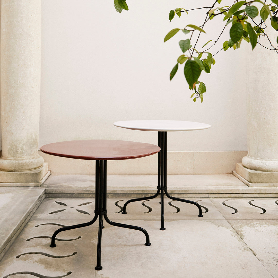 Two round tables in deep red and crisp white with black metal bases, set against a simple, elegant backdrop.