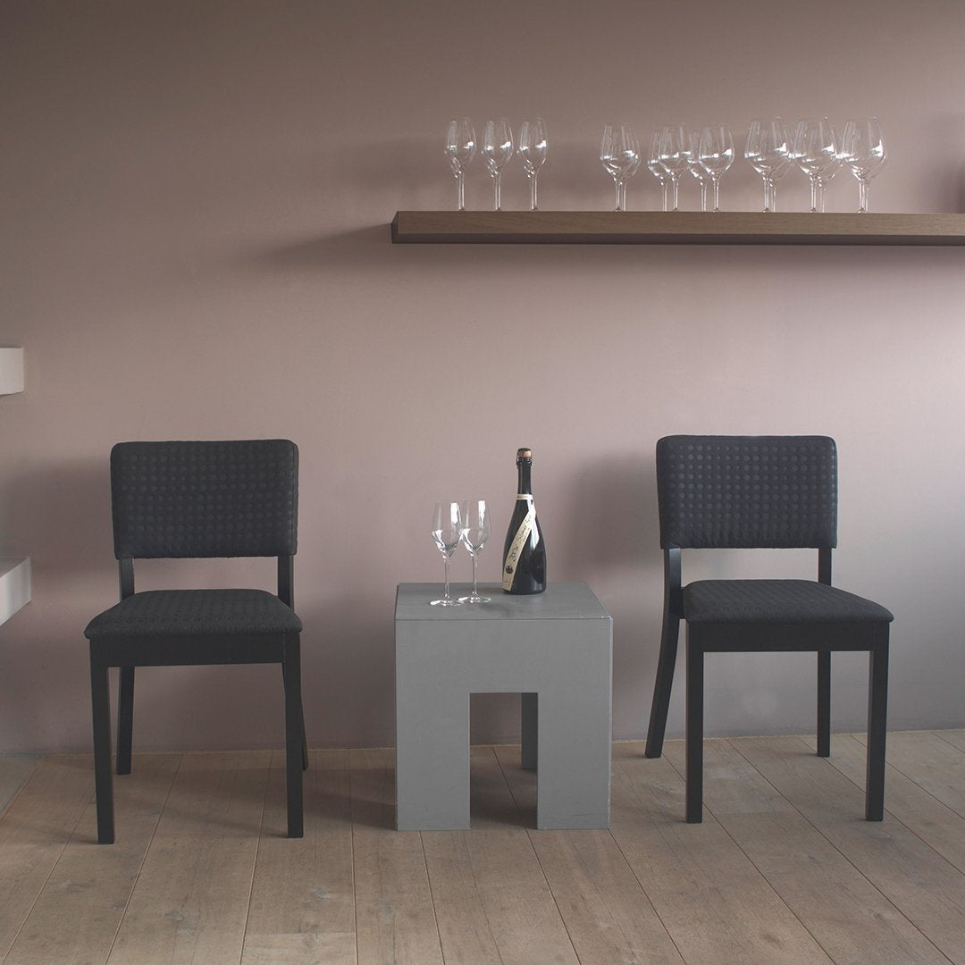 Black woven chairs with a sleek gray table in a minimalist setting, accented by soft beige walls. Perfect for modern decor.