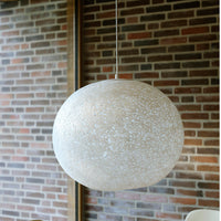 Textured cream pendant light with a speckled finish, complementing a rustic brick backdrop. Elegant and modern design.