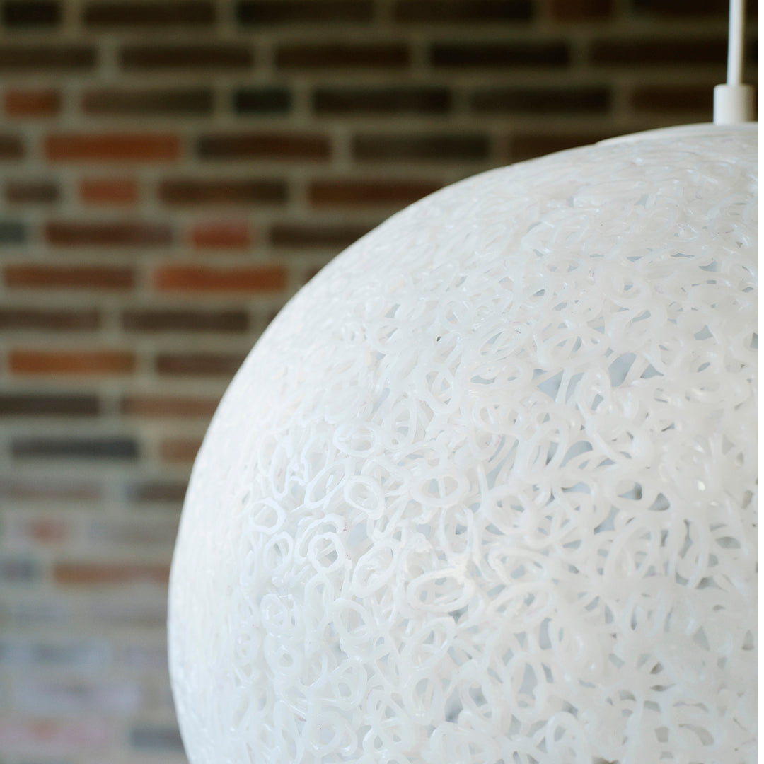 White pendant lamp with intricate lace-like patterns, set against a rustic brick wall backdrop.