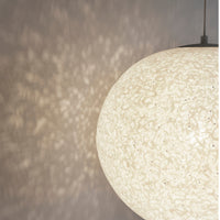 "Round white pendant lamp casting intricate, textured patterns on a soft gray wall."