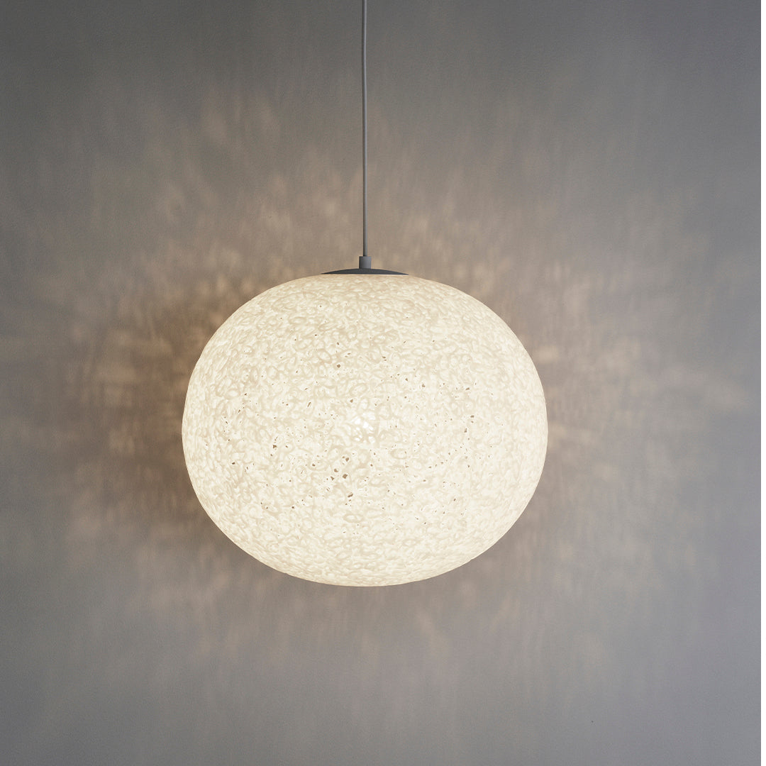 "Round white pendant light with textured pattern, casting soft shadows against a gray wall."