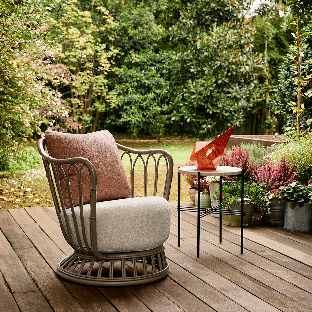 "Cozy outdoor chair featuring a soft brown pillow and white cushion on a natural wood deck, complemented by vibrant plants."