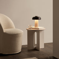 Beige textured chair, black and cream lamp, wooden table with a light-colored top, and warm earthy tones.