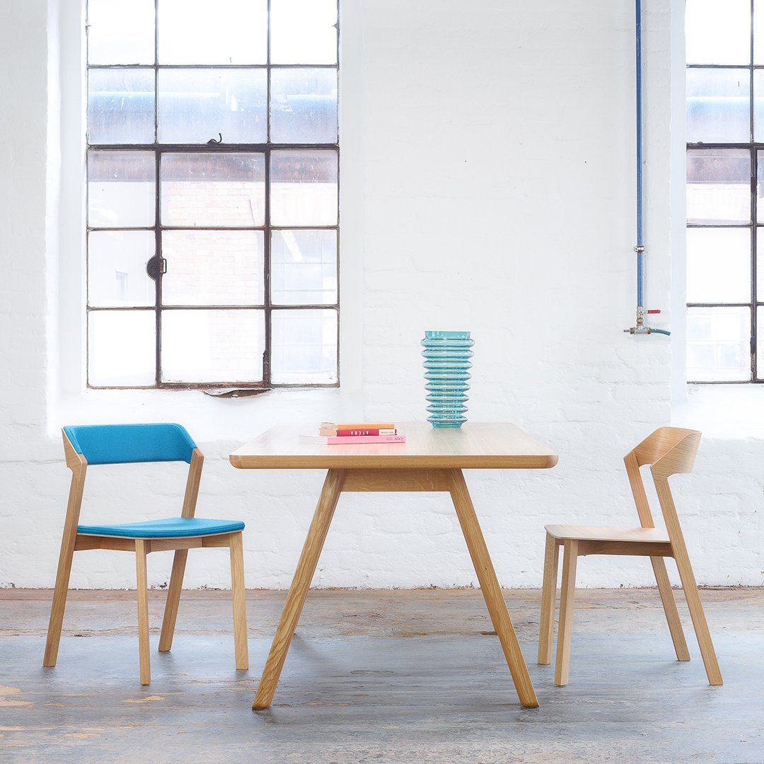 Modern wooden table with light wood finish, paired with blue and natural wooden chairs; stacked turquoise bowls.