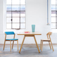 Modern wooden table with light wood finish, paired with blue and natural wooden chairs; stacked turquoise bowls.