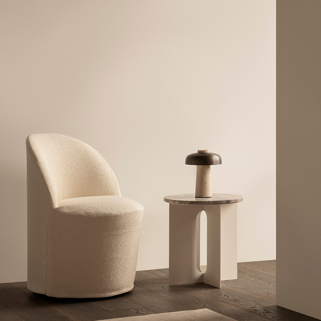 Cream textural chair alongside a beige side table and a brown lamp, set against soft neutral tones.