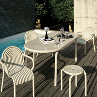 Beige dining table and chairs with ribbed patterns, set against a textured wooden deck and a blue pool background.
