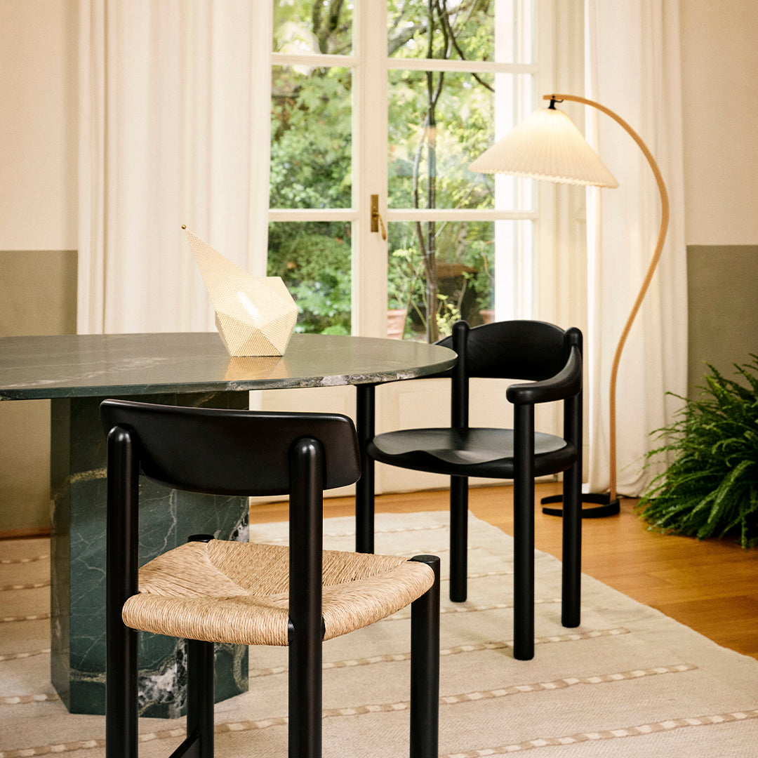 Black chairs with woven seats beside a green marble table, against earthy tones and soft neutral patterns.