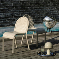 Beige chairs with ribbed patterns beside a silver sculpture and glassware on a wooden surface near a pool.