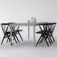 Light wood dining table with sleek black chairs, featuring a minimalist design and modern color contrast.
