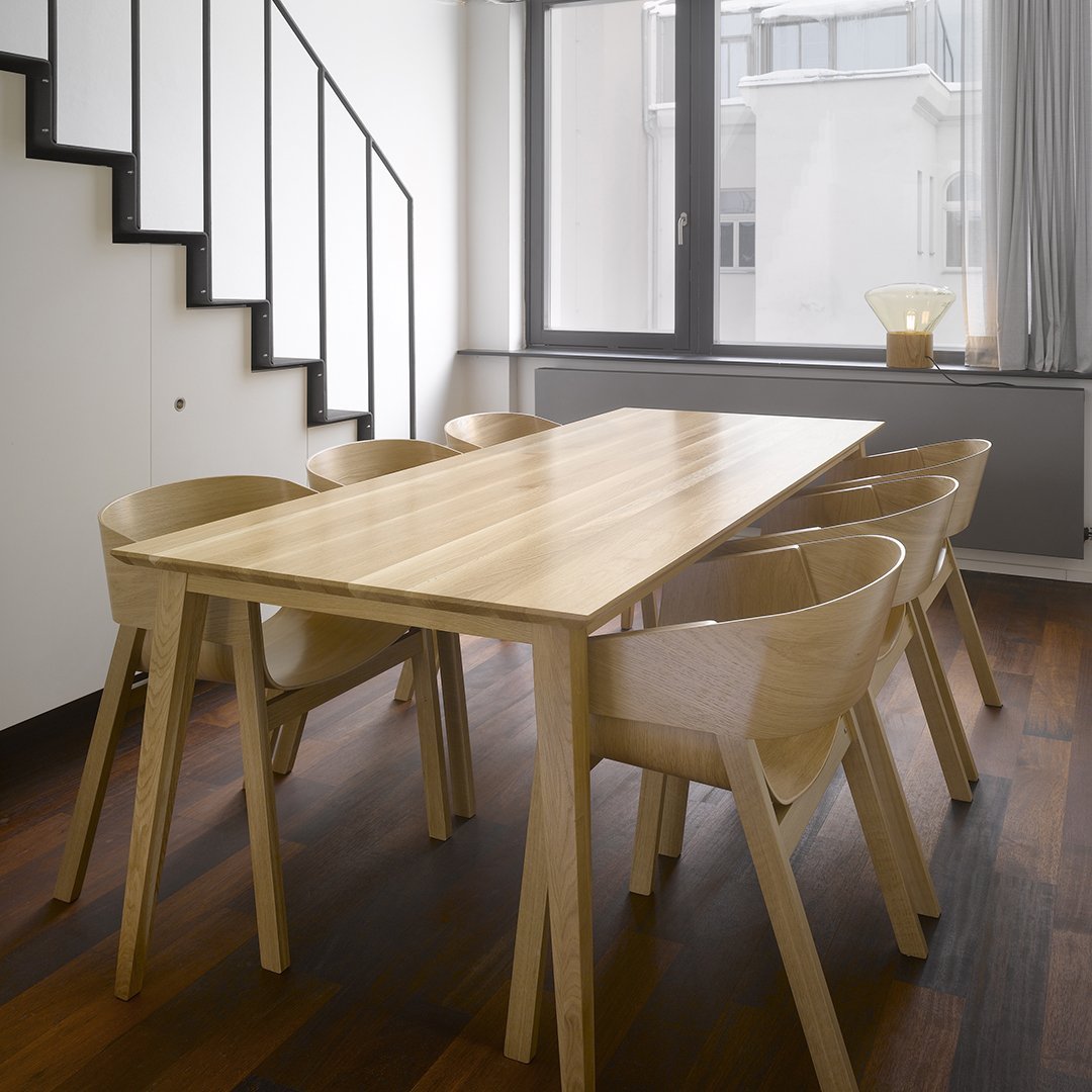 Natural wood dining table with light beige chairs, set against a modern interior featuring white walls and warm wood floors.