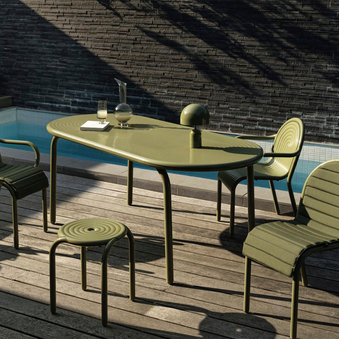 Green outdoor dining set with ribbed patterns, including a table and chairs, against a textured stone wall.