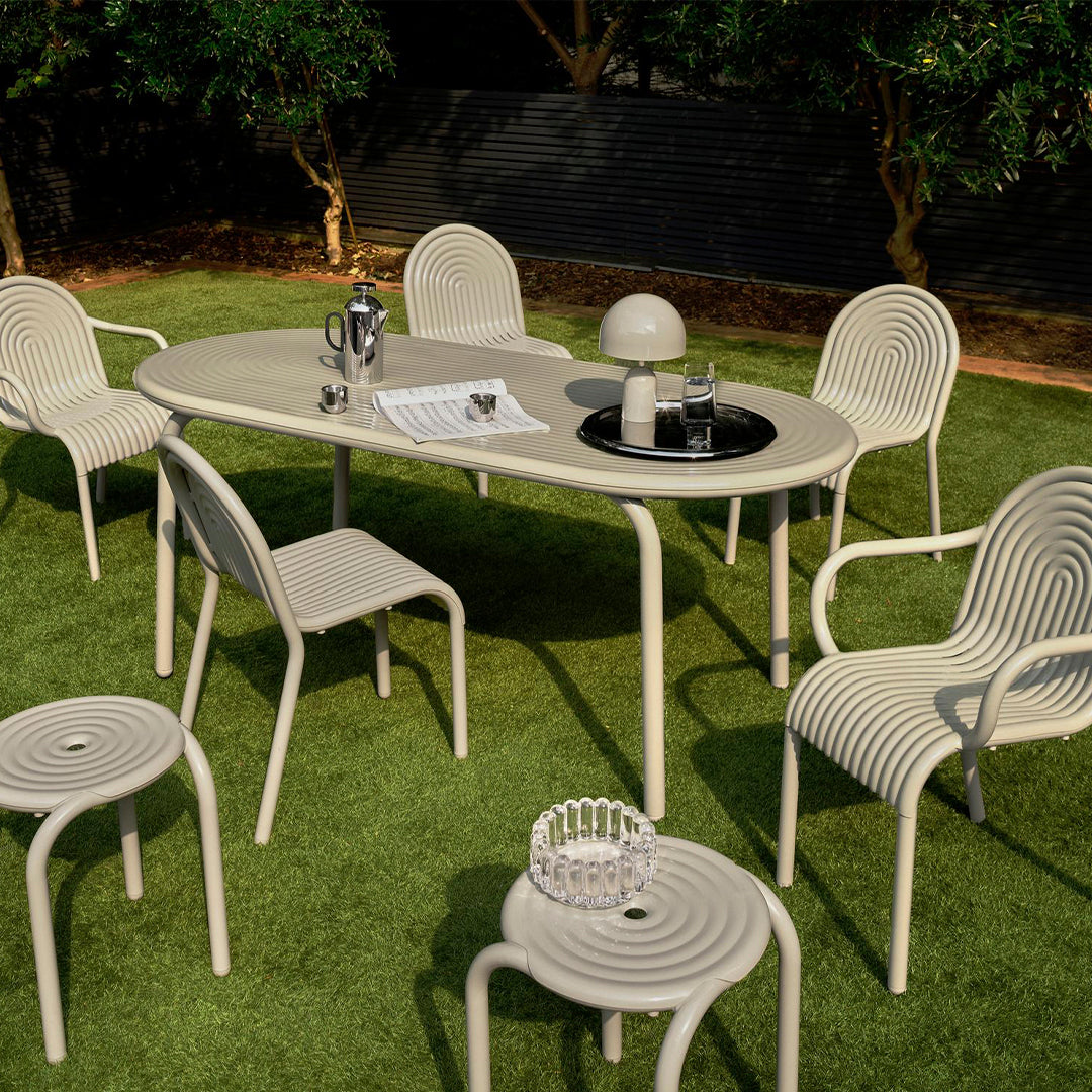 Modern outdoor dining set featuring soft beige furniture with subtle ribbed patterns on a lush green lawn.