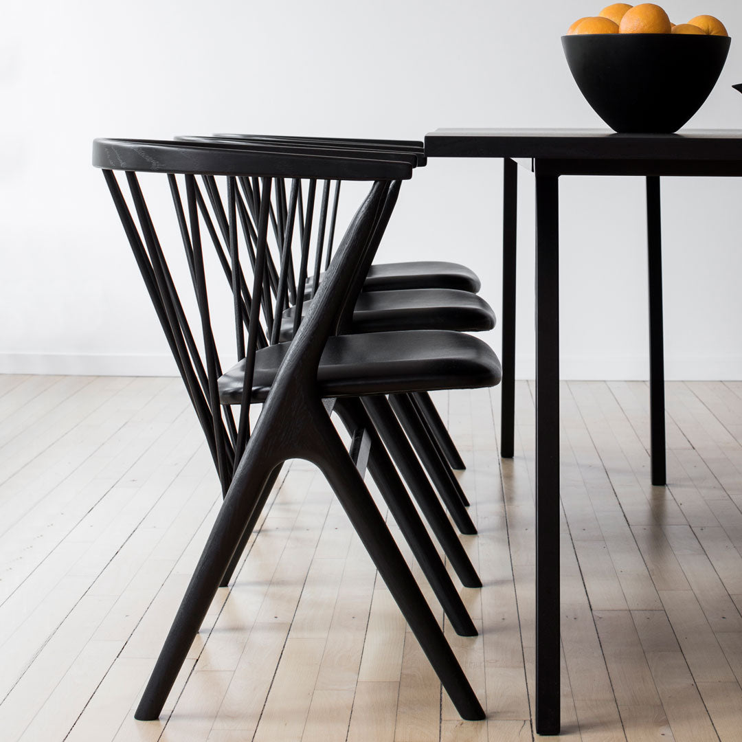 Black dining chairs with geometric patterns, paired with a sleek black table and a bowl of oranges.