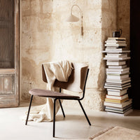 Modern chair in soft beige and brown tones, featuring a minimalist design and textured fabric against rustic stone walls.