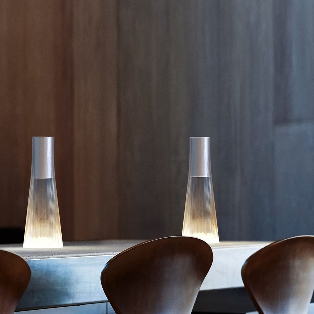 Sleek glass water carafes with gradient light, set against a warm wood backdrop and modern wooden chairs.