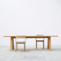 Light oak dining table with minimalist design, complemented by beige upholstered chairs against a neutral background.