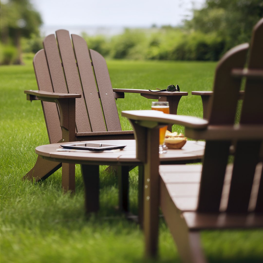 "Brown wooden Adirondack chairs and circular table on green grass, creating a cozy outdoor seating area."