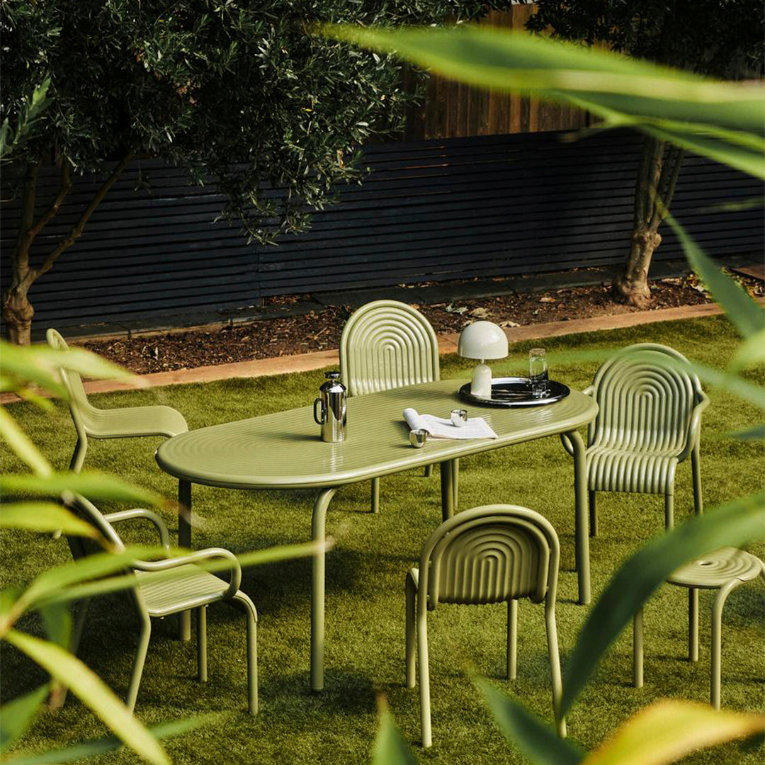 Green outdoor dining set featuring ribbed patterns on chairs and table, set on lush grass. Modern, fresh aesthetic.
