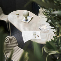 Stylish beige dining table with ripple pattern, surrounded by soft gray chairs, accented by a green lamp and decor.