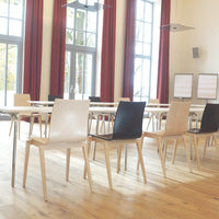 "Modern chairs in black and white with natural wood legs, arranged in a bright, spacious room with wooden floors."