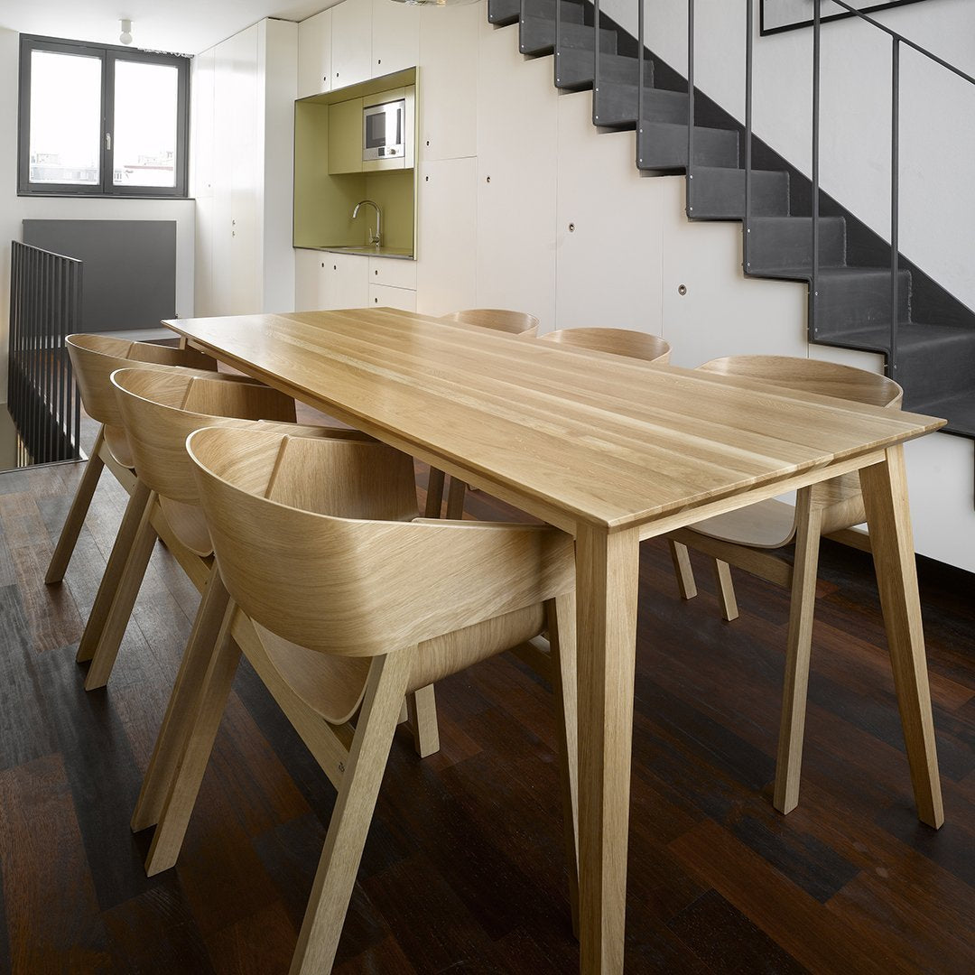 Natural wood dining table with light beige finish and matching light beige chairs on a dark wood floor.