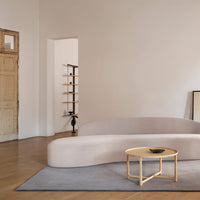 Stylish soft gray sofa with a round wooden coffee table on a muted gray rug in a minimalist interior.