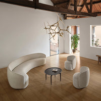 Curved beige couch and round black table on warm wooden floor in a minimalistic interior with natural light.