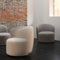 Modern gray upholstered chairs against a textured brick wall, featuring neutral tones and soft, rounded forms.