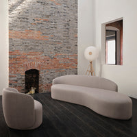 Soft beige curved sofa and chair against a textured gray and red brick wall, complemented by dark wood flooring.