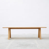 Natural wooden table with a smooth light oak finish and minimalist design, showcasing clean lines and a subtle grain pattern.