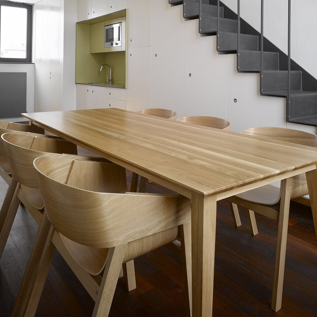 Natural wood dining table with light beige finish, surrounded by matching wooden chairs on dark wooden floor.