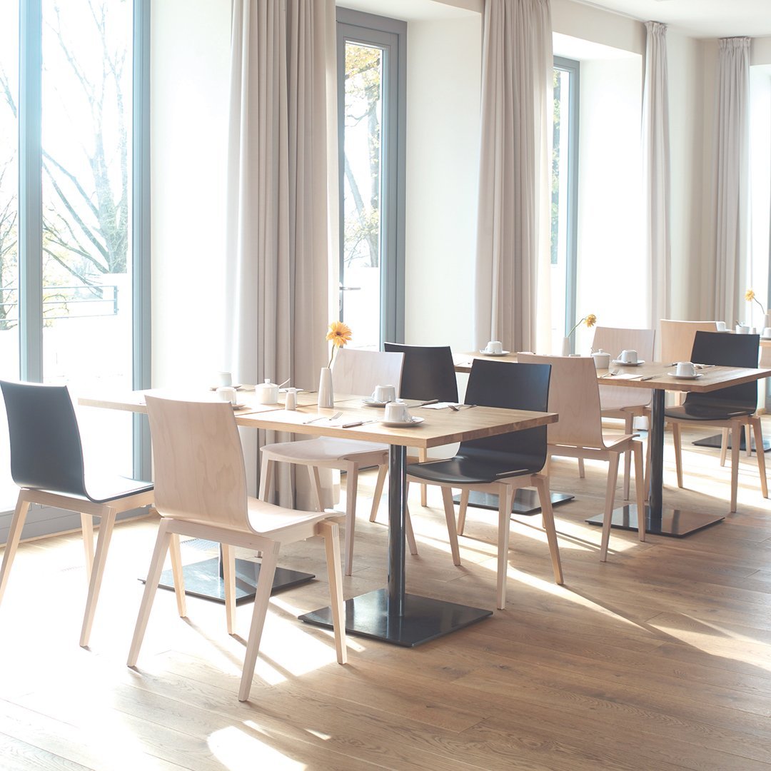 "Modern dining area featuring light wood chairs with black and beige upholstery, complemented by soft beige curtains."